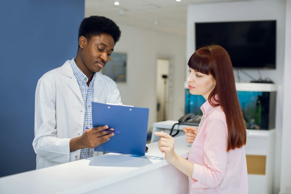 Male afro-american receptionist, standing at the desk, taking application form from female client