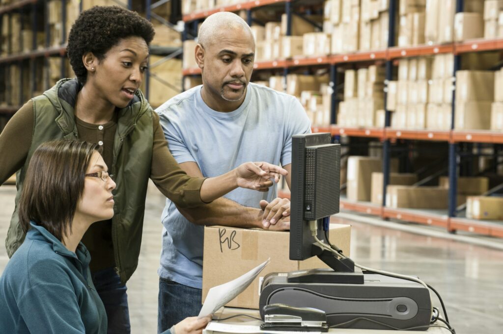 Warehouse workers checking inventory on a computer in a large distrubiton warehouse.