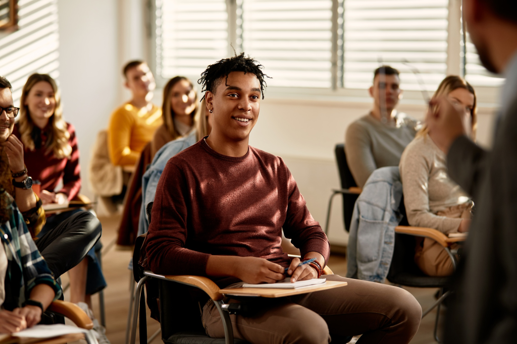 Students engaged in a classroom lecture, smiling and paying attention to the instructor