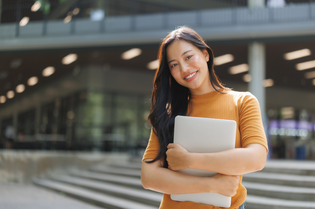 SACC Career Center student standing outside campus building holding laptop and smiling confidently